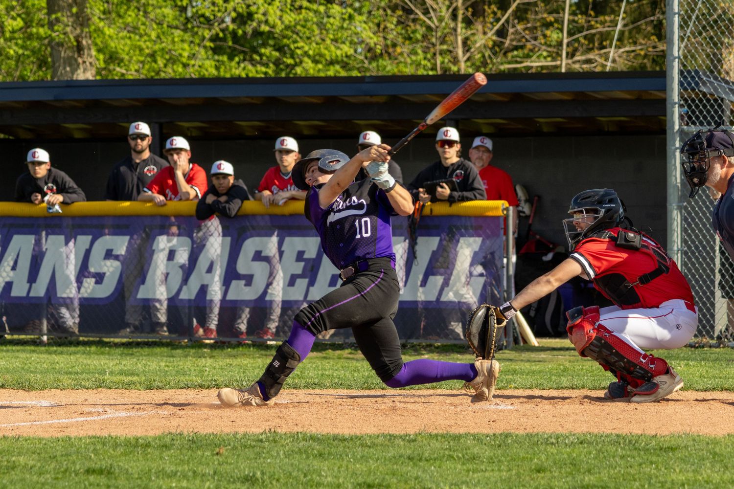 Baseball player in purple uniform number 10 swinging bat during competitive game.