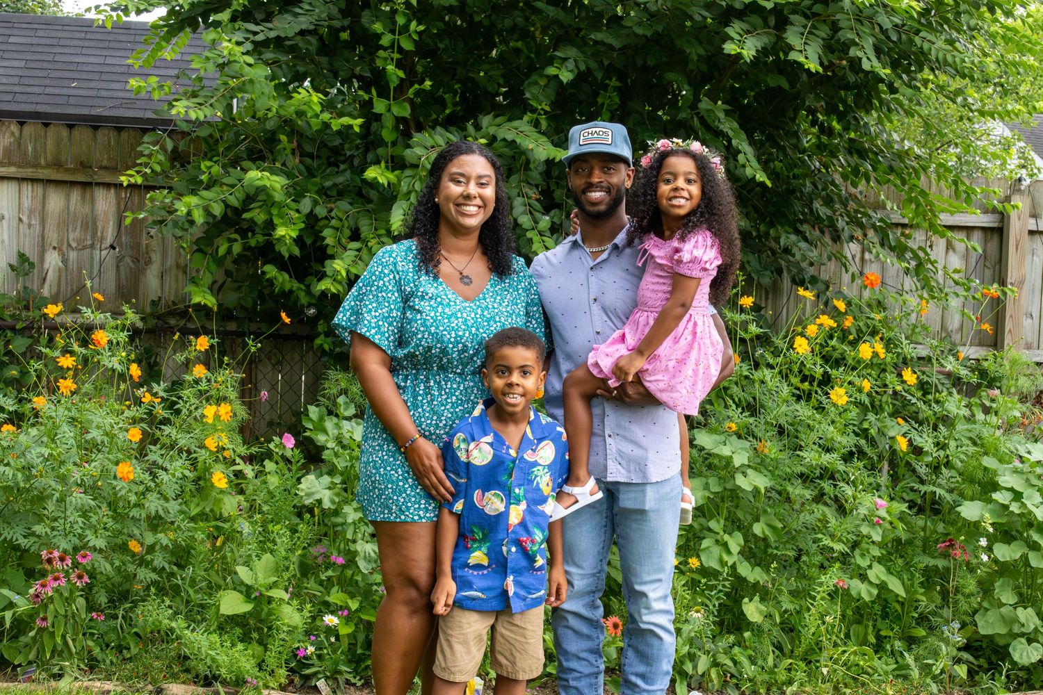 A happy family of four, including two young children, poses together in a vibrant backyard garden in summer.