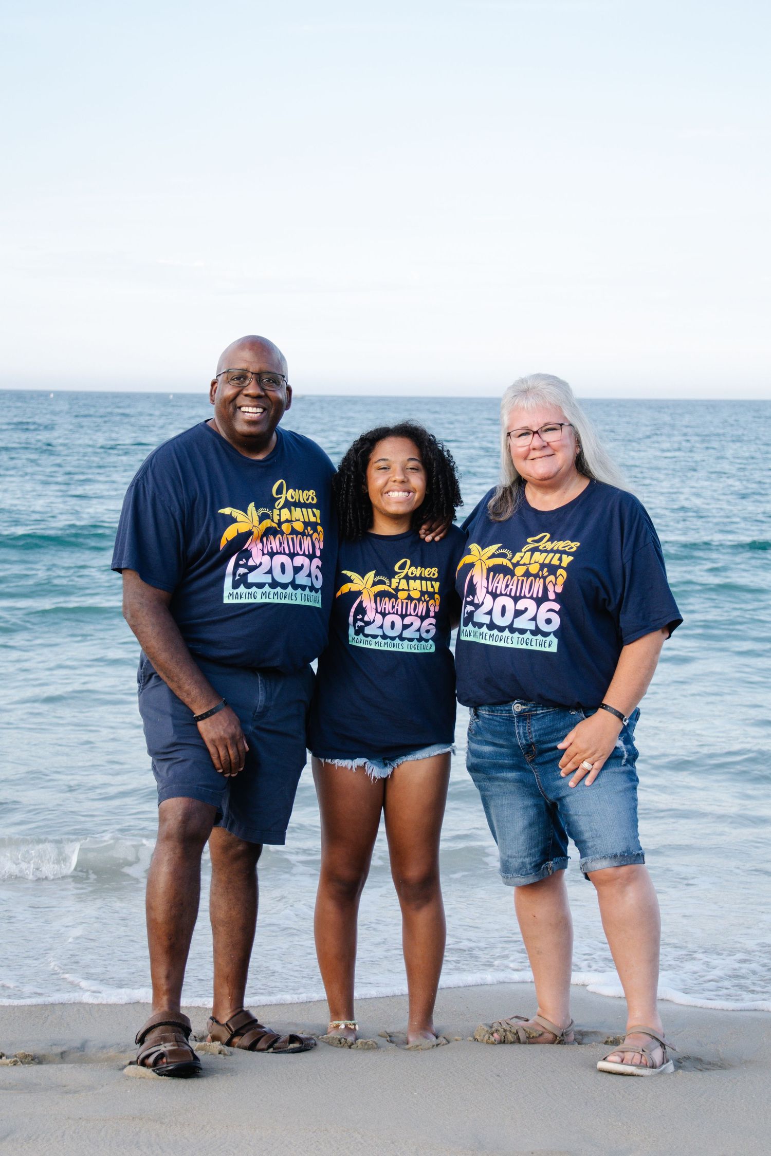Family of three wearing matching navy family reunion 2025 shirts posing on a beach.