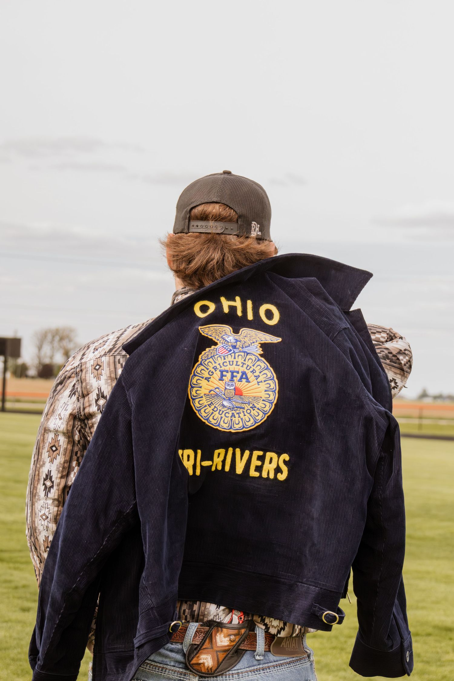 Student wearing Ohio FFA Tri-Rivers chapter jacket viewed from behind on an open field.