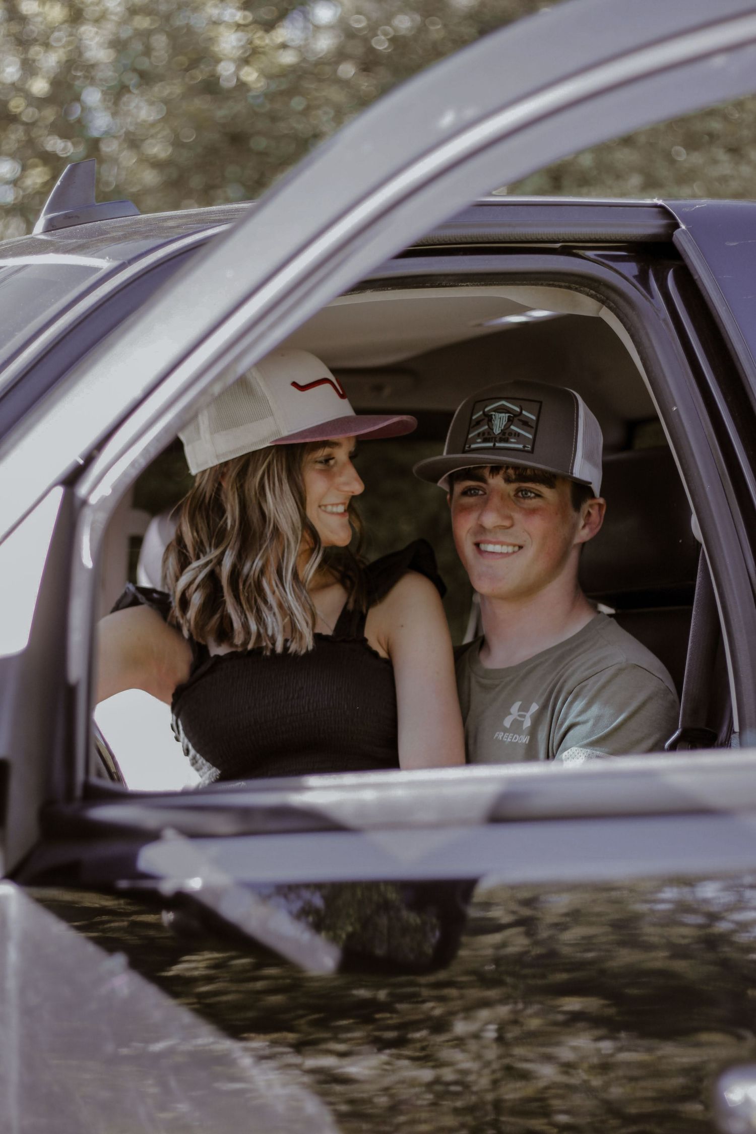 Smiling couple in trucker hats sitting together inside a pickup truck cab.
