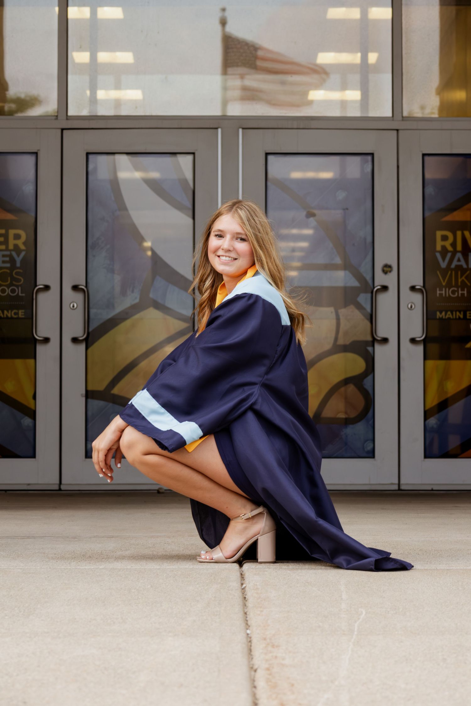 Smiling female graduate in navy gown posing outside River Valley Vikings High School entrance.