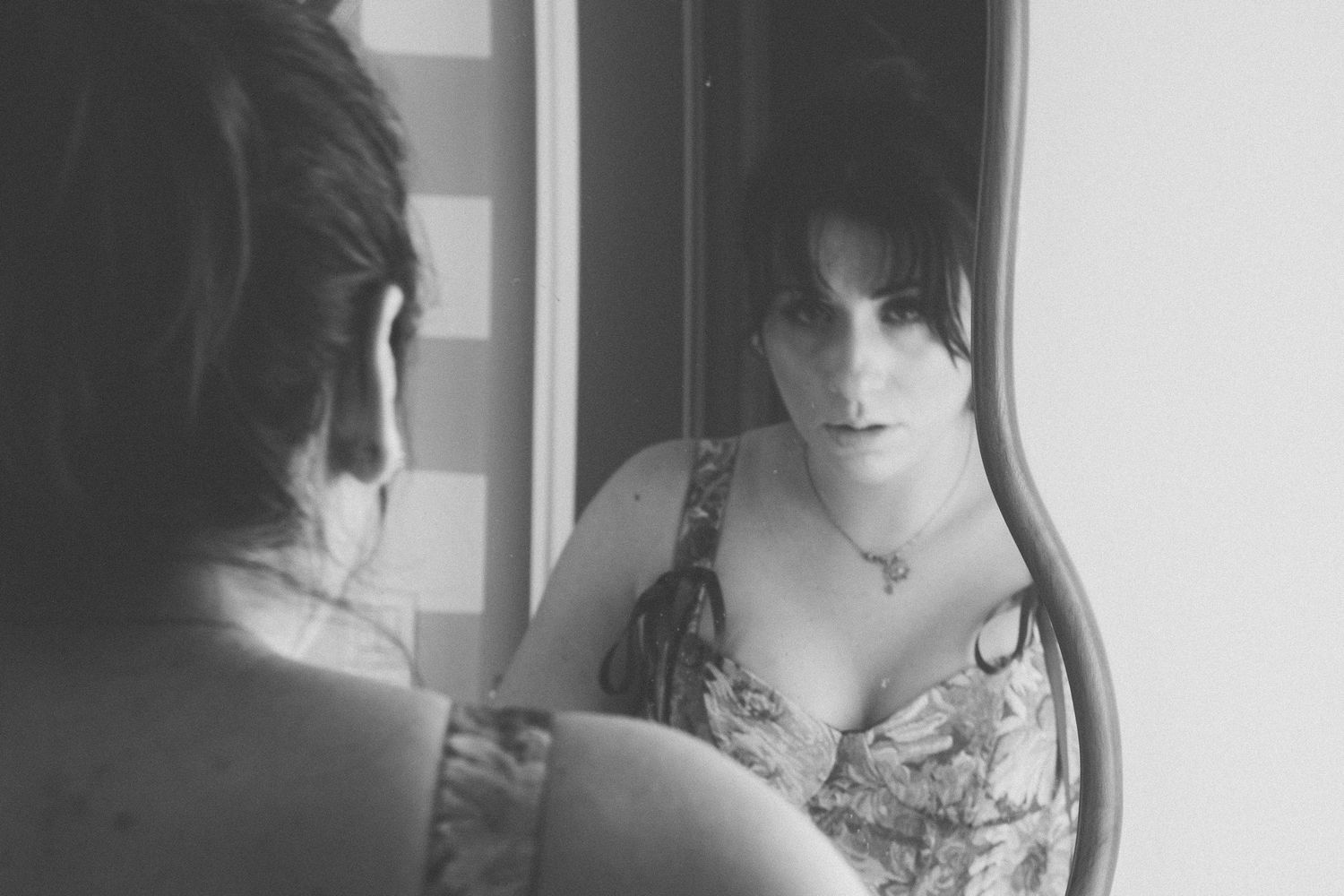 Portrait en noir et blanc d'une femme contemplant son reflet dans un miroir orné.