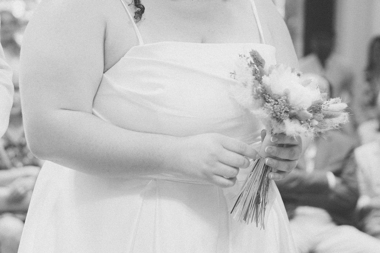 Photo en noir et blanc d'une mariée en robe blanche tenant un bouquet de fleurs séchées bohème.