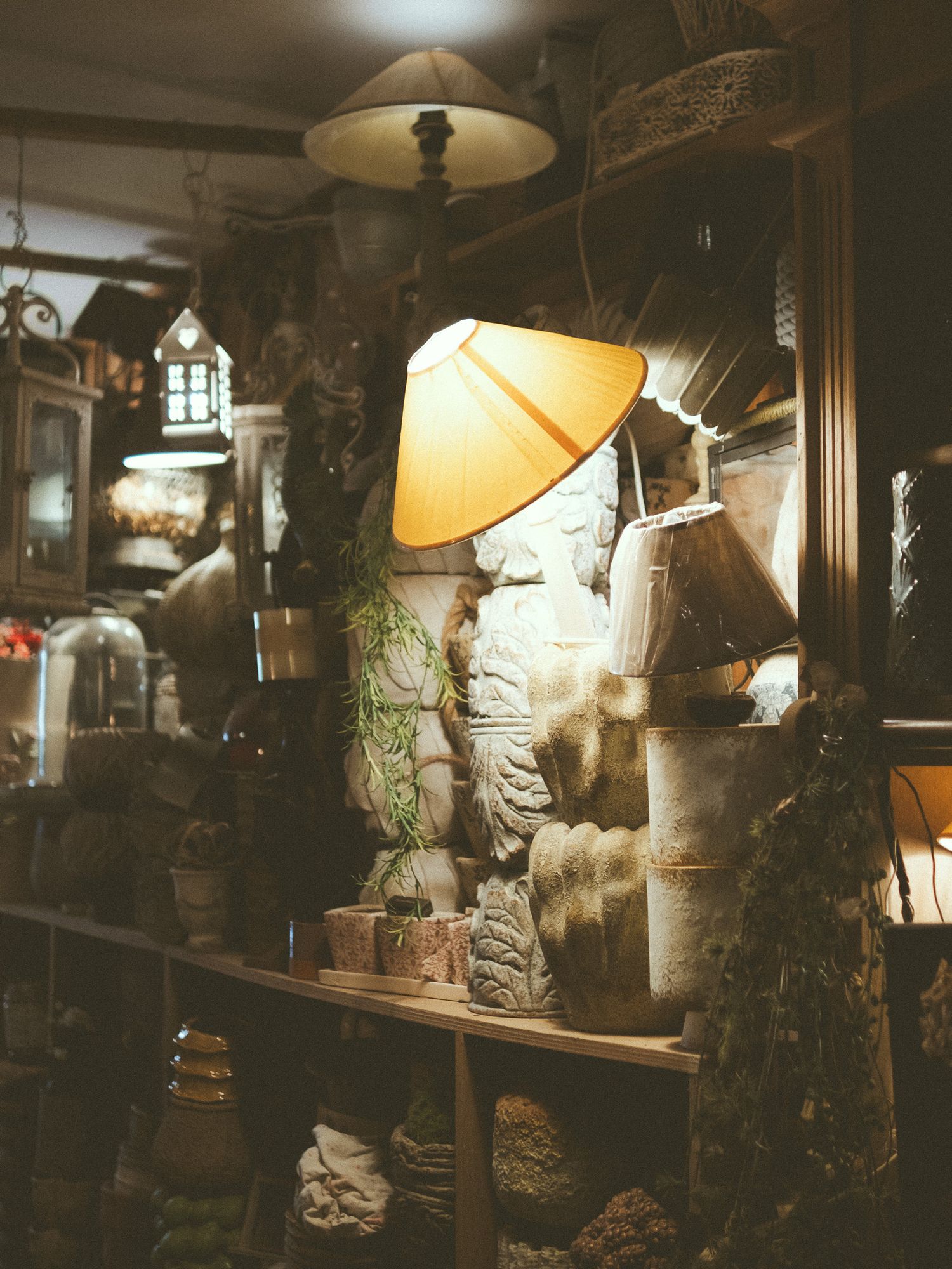 Warm glowing lamp illuminating stone sculptures and artifacts on wooden shelves in an antique shop.