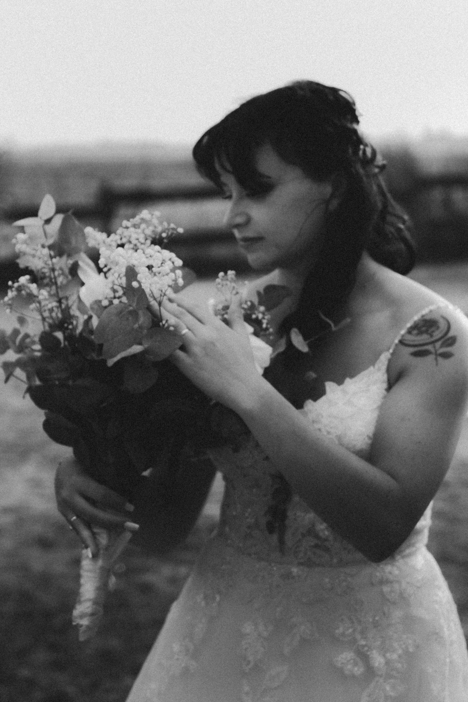 Bride in lace gown smelling her wedding bouquet in a black and white portrait photo.
