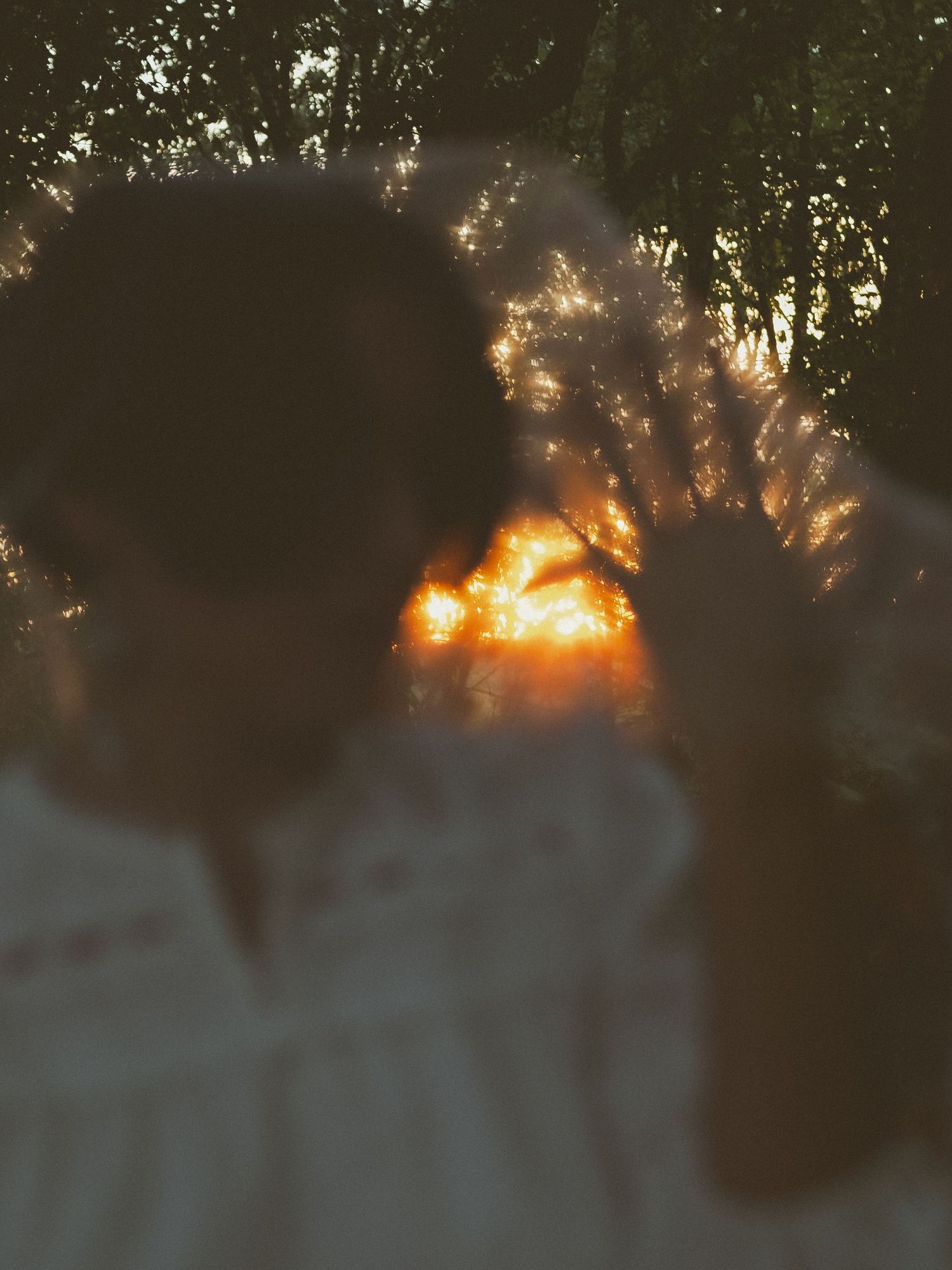 A dreamy blurred silhouette of a person with golden sunset light glowing through trees in the background.