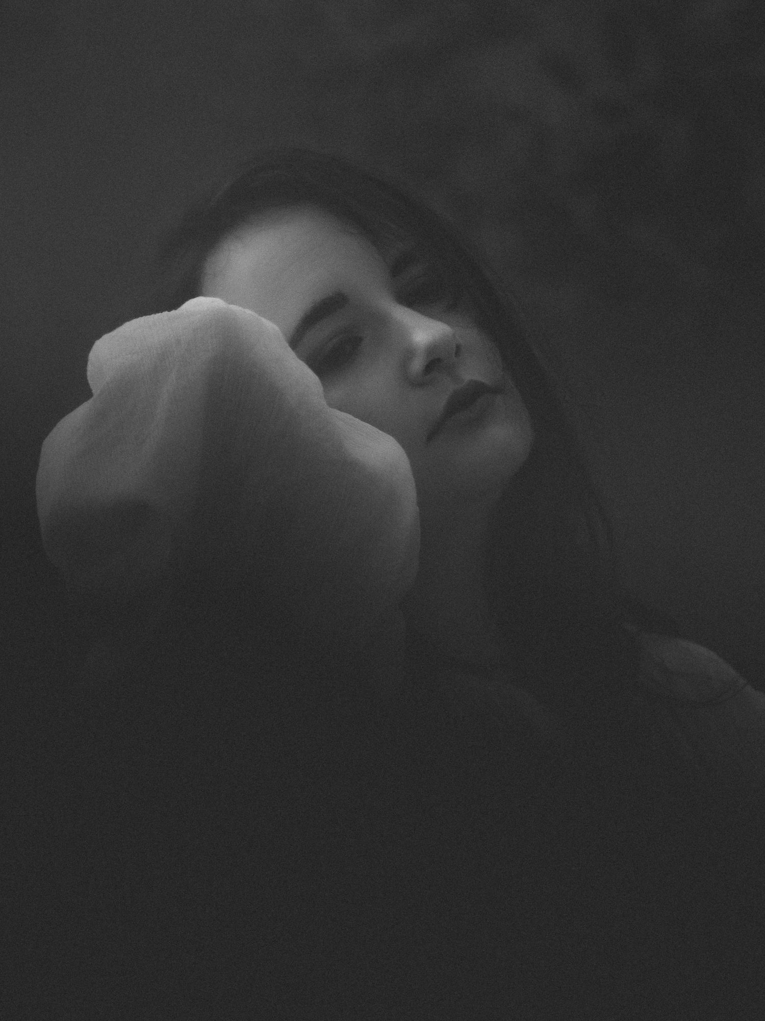 Black and white portrait of a young woman resting her face against her raised fist with closed eyes.