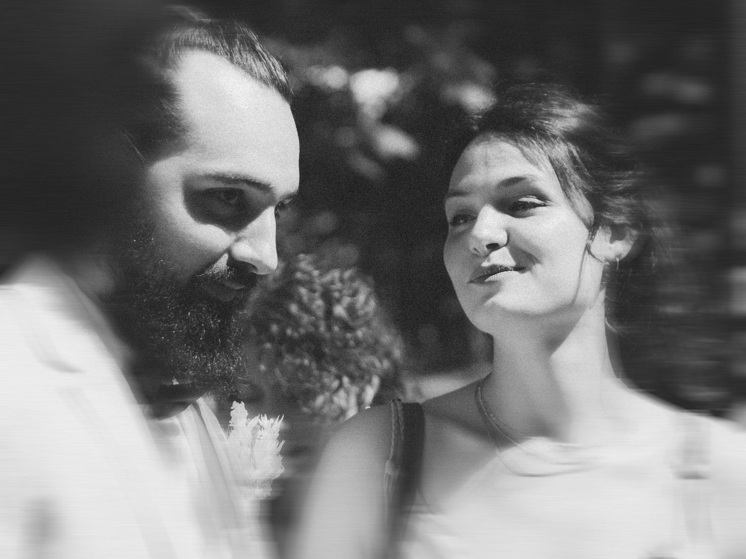 Photo en noir et blanc d'un marié barbu et d'une mariée souriante partageant un moment tendre.