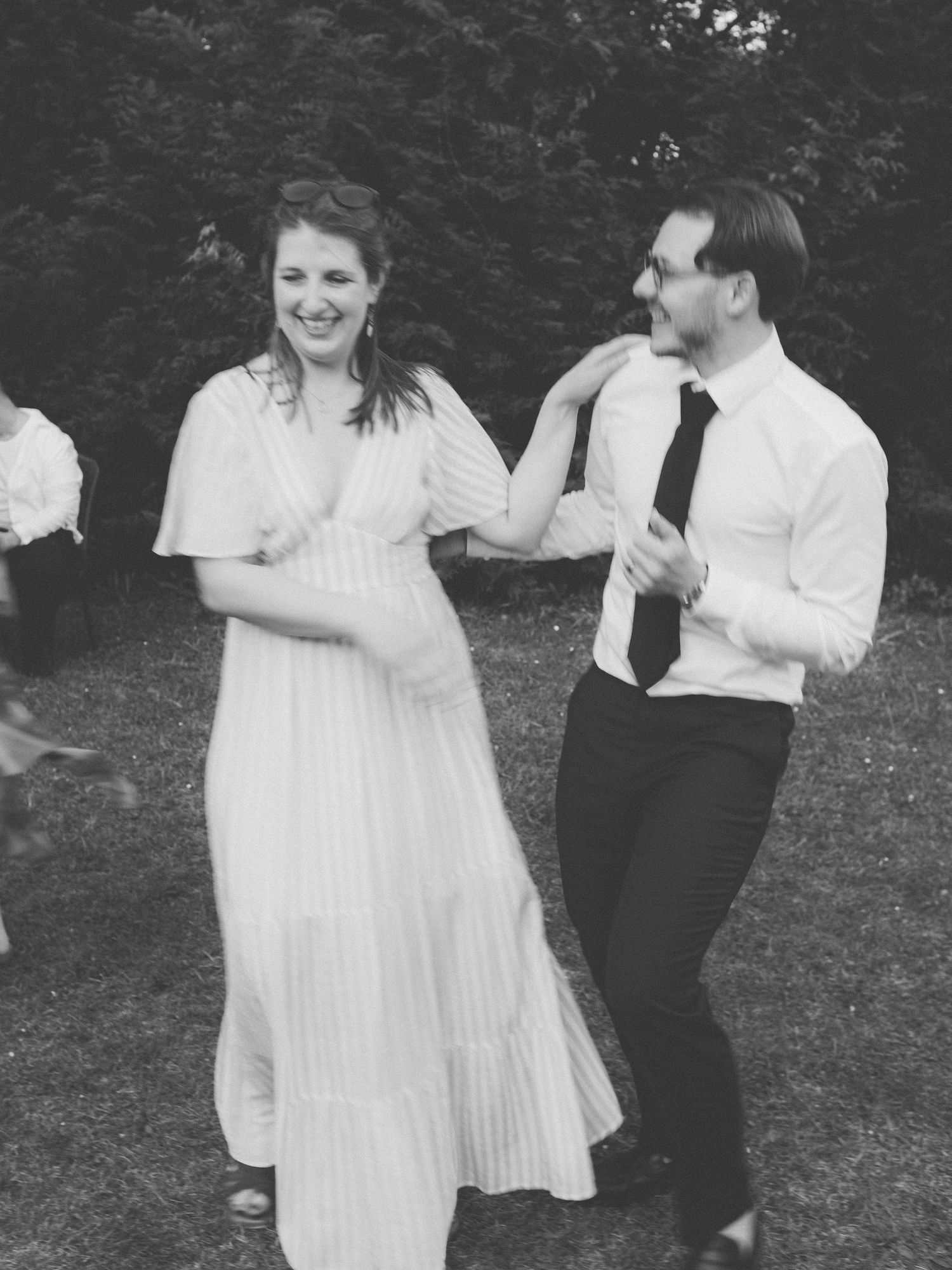 Couple dancing joyfully outdoors at a wedding reception, woman in white dress, man in white shirt and tie.
