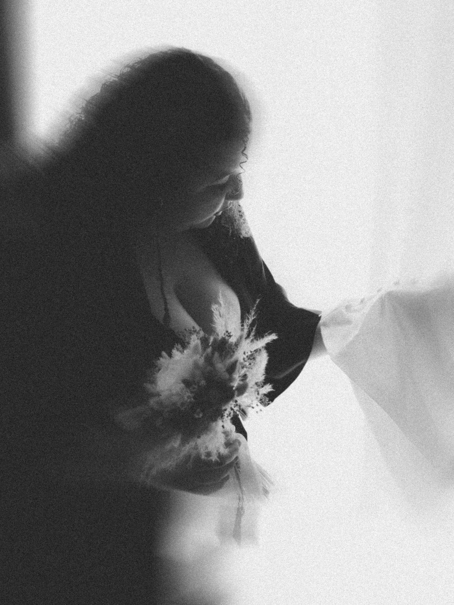 Silhouette dramatique en noir et blanc d'une mariée avec bouquet sur fond blanc lumineux.