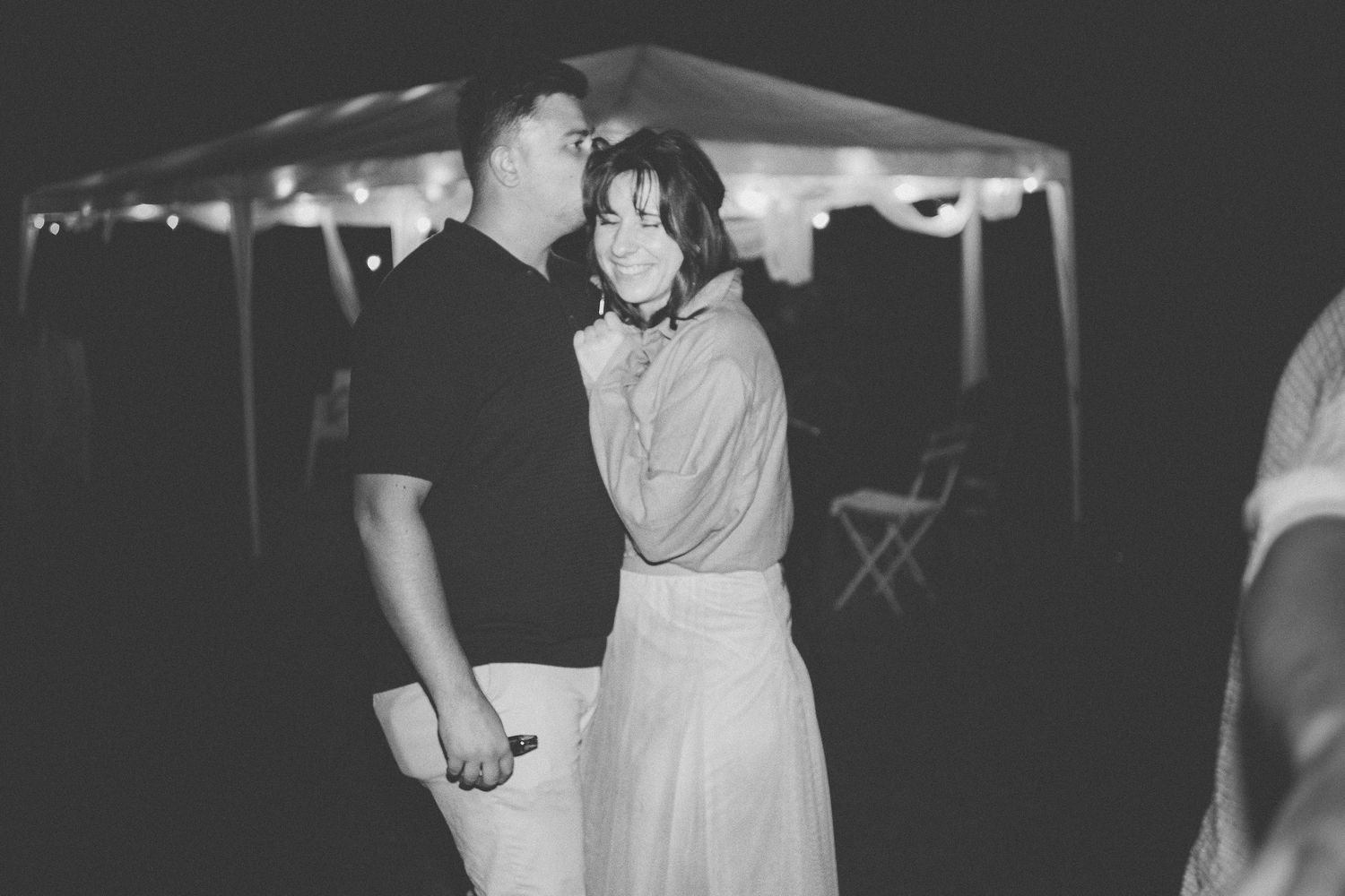 Photo en noir et blanc d'un couple dansant lentement lors d'une réception de mariage en plein air le soir.