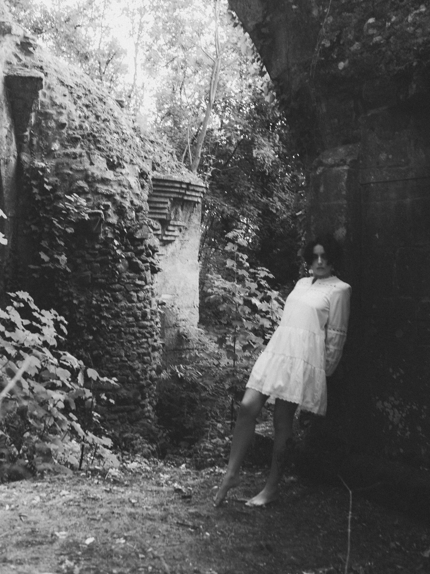 Black and white photo of woman in white dress standing in ancient ruins.