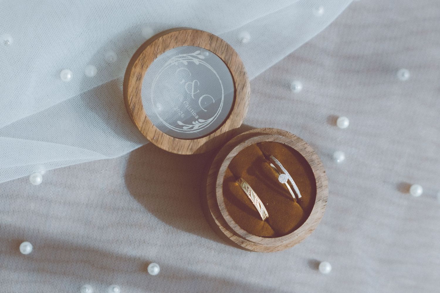 Alliances présentées dans une boîte en bois rustique sur un voile blanc avec des accents de perles.