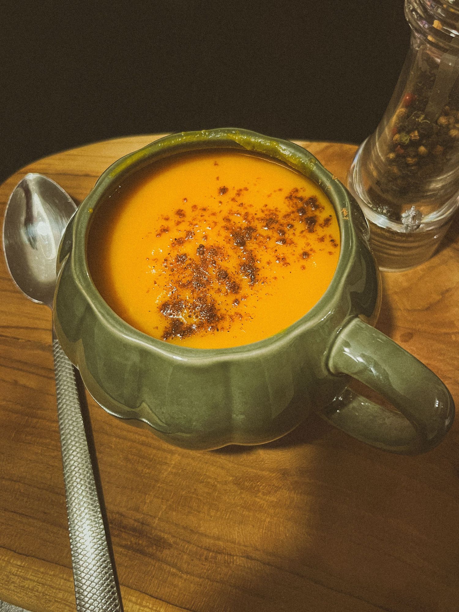 A vibrant orange butternut squash soup in a green ceramic mug, topped with spices, served on a wooden board.
