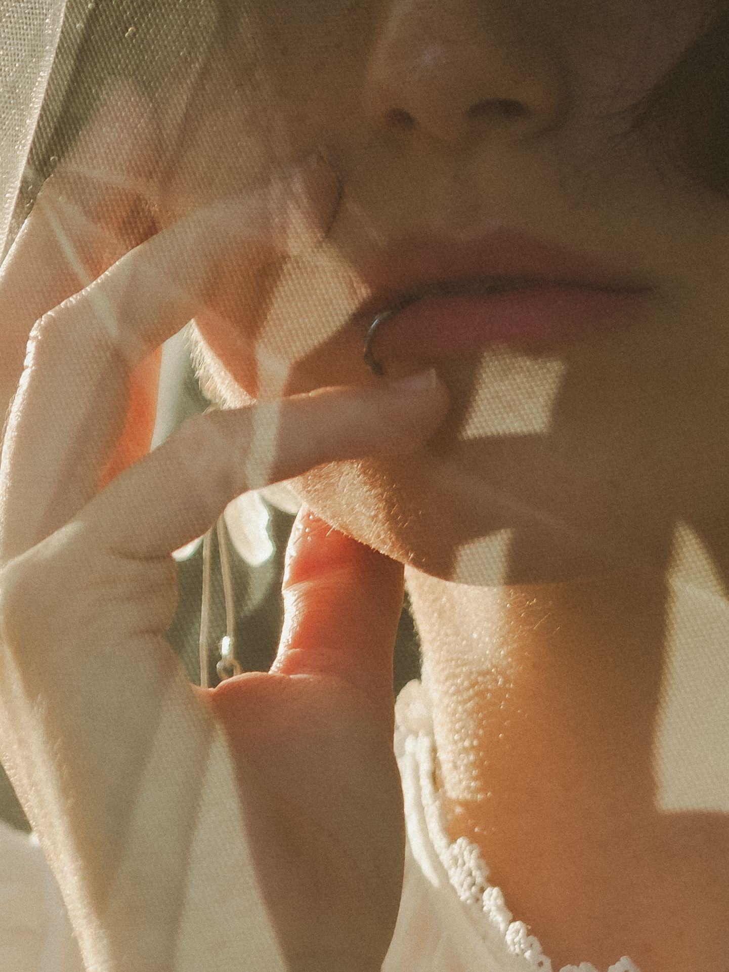 Close-up of a person touching their lips with fingers, wearing a ring, soft warm lighting.