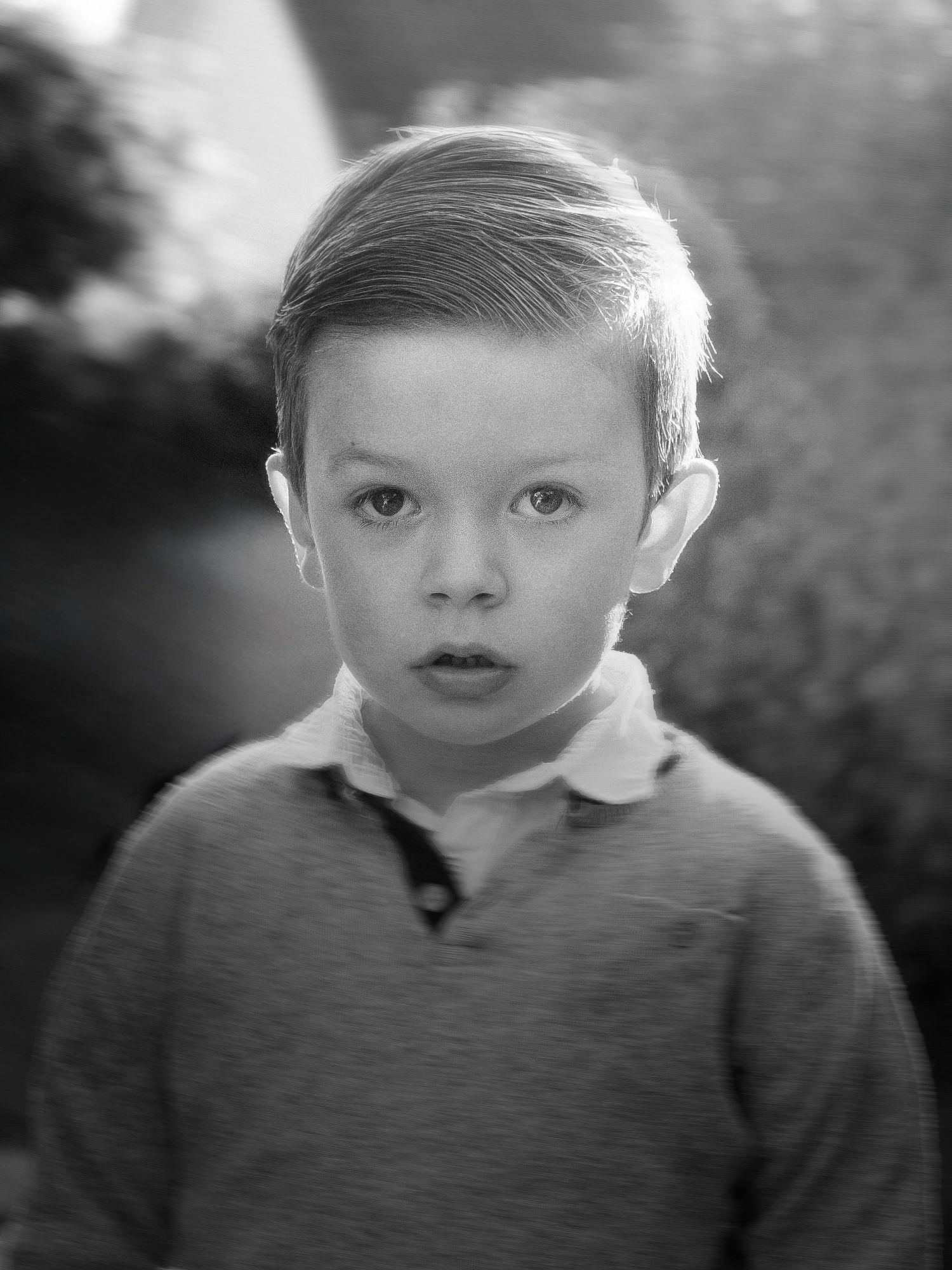 Portrait en noir et blanc d'un jeune garçon aux cheveux soignés portant un pull à col en extérieur.