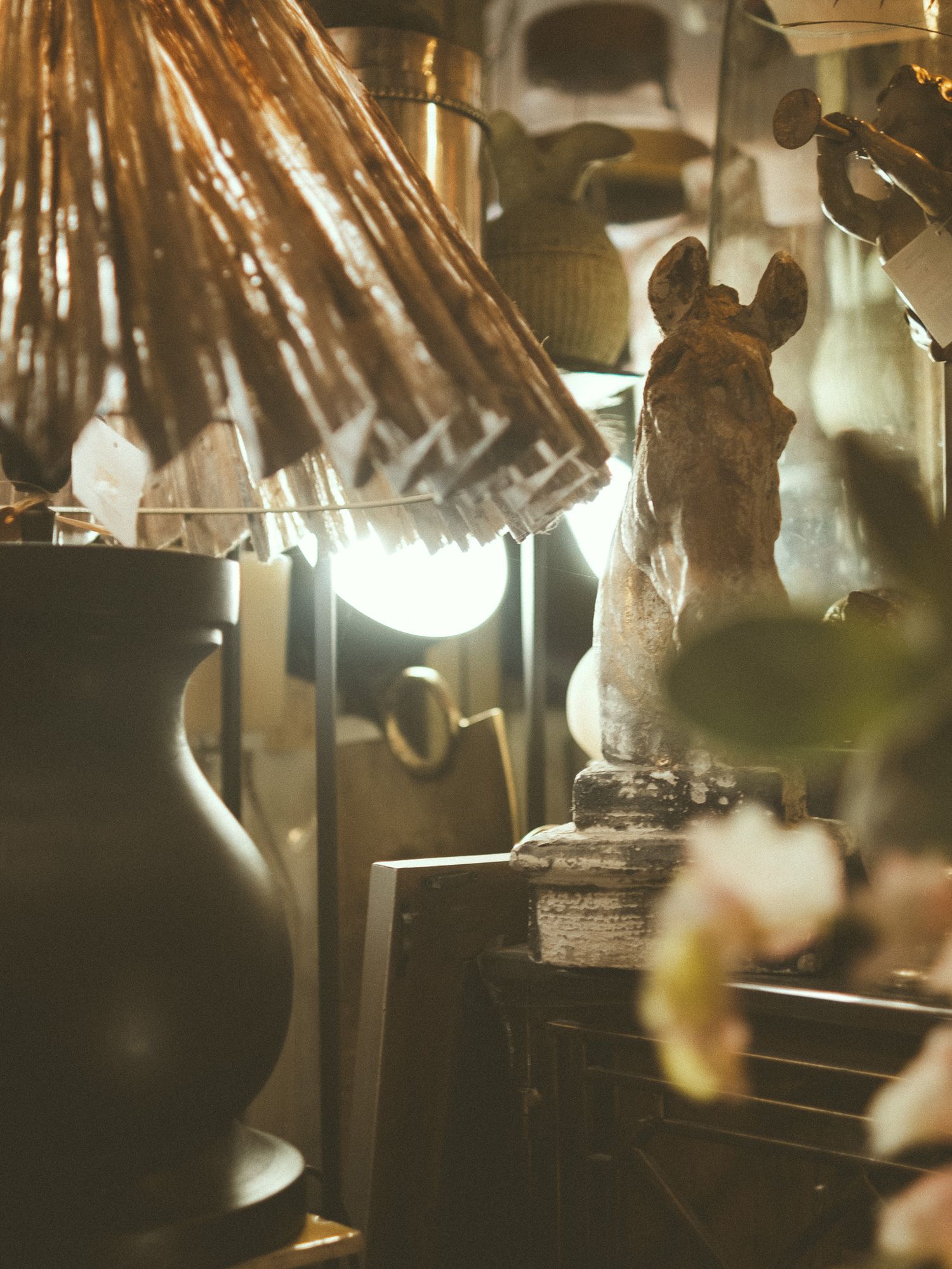 Vintage eclectic shelf display with horse bust sculpture, glowing lamp, ceramic vase, and dried botanicals in warm golden light.
