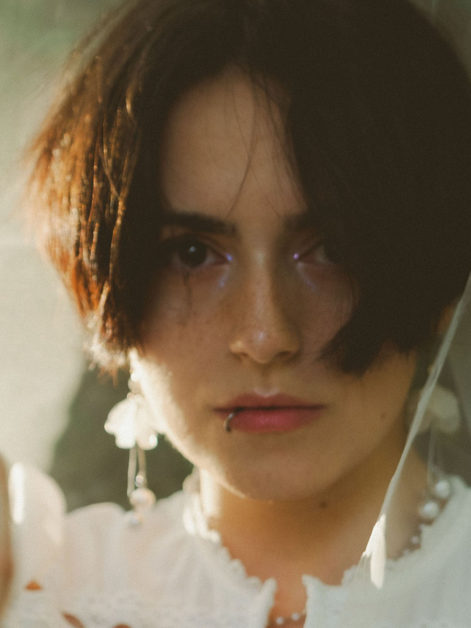Close-up portrait of young woman with short dark hair wearing floral drop earrings.