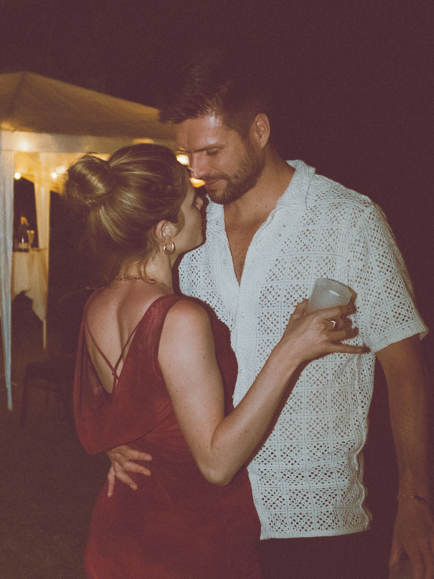 Couple partageant un moment romantique lors d'une réception de mariage en extérieur sous des lumières chaudes.