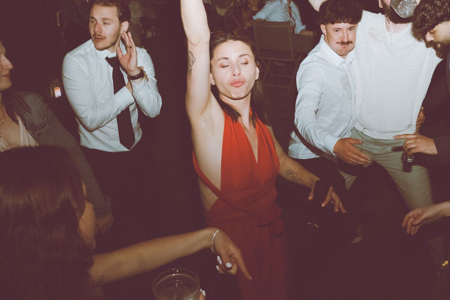 Femme en robe rouge dansant le bras levé lors d'une réception de mariage animée.