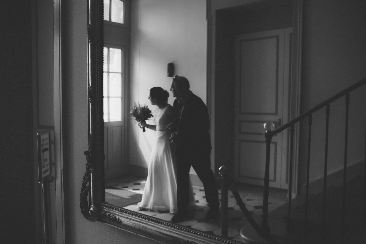Black and white photo of a bride and groom sharing a romantic moment by a window on a staircase landing.