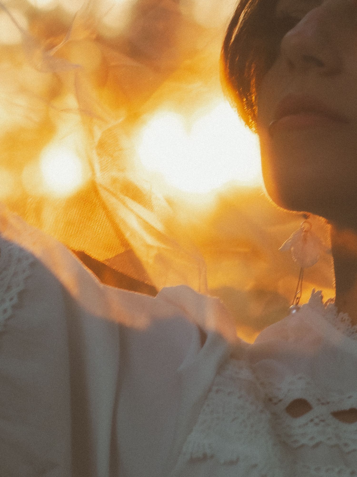 A woman in white lace bathed in warm golden sunset light, with soft bokeh and ethereal glow in the background.