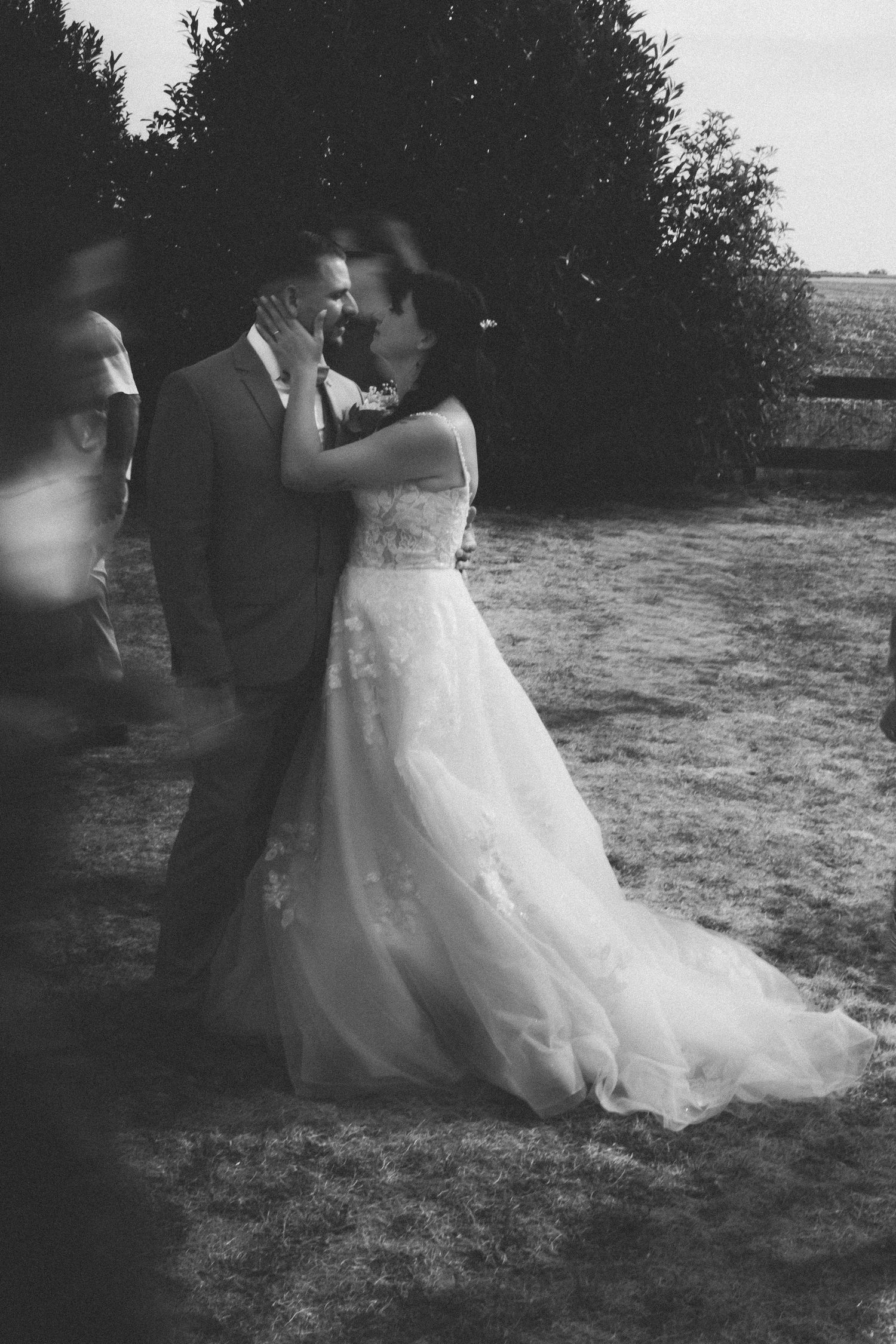 Black and white photo of a bride and groom sharing a kiss outdoors on their wedding day.