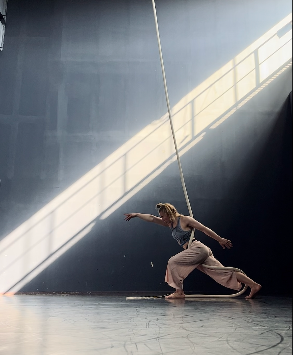 aerial artist Adela Jordakova in lunge with rope wrapped around her body, pointing in front of her with dramatic background