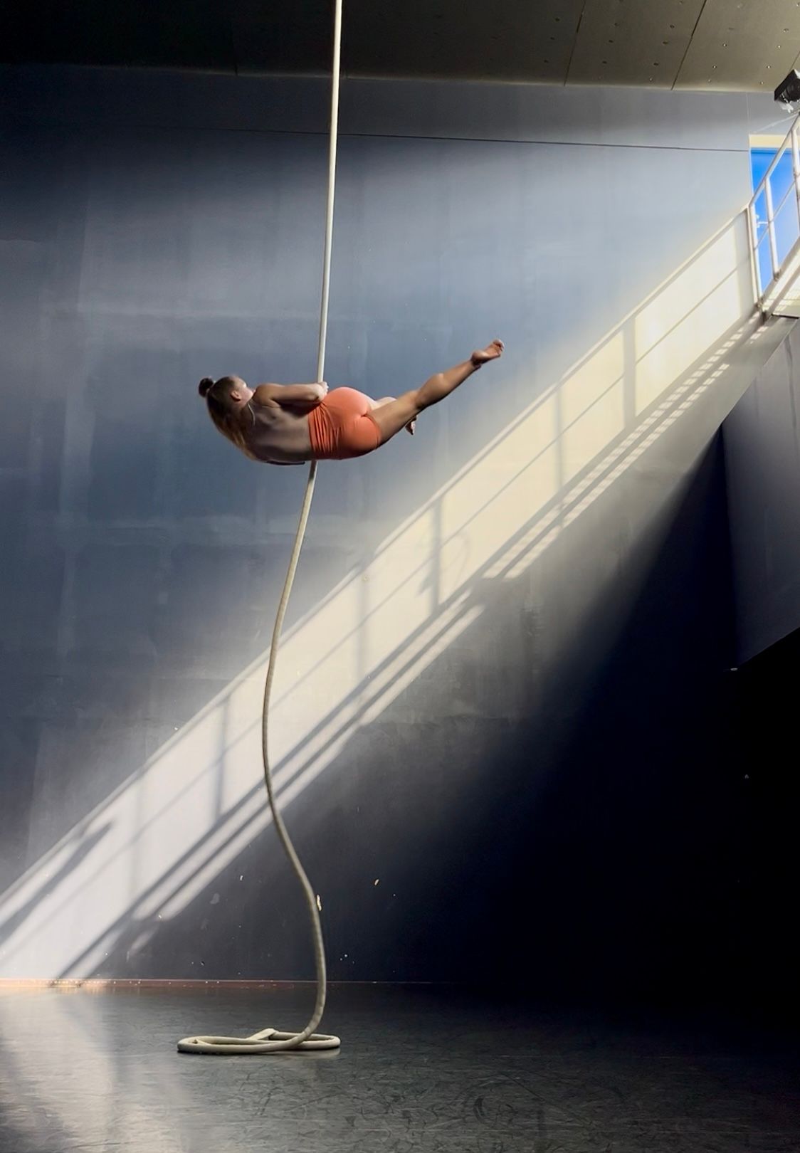 Aerial rope artist Adela Jordakova doing dynamic move mid-air, silhouetted in a diagonal beam of light