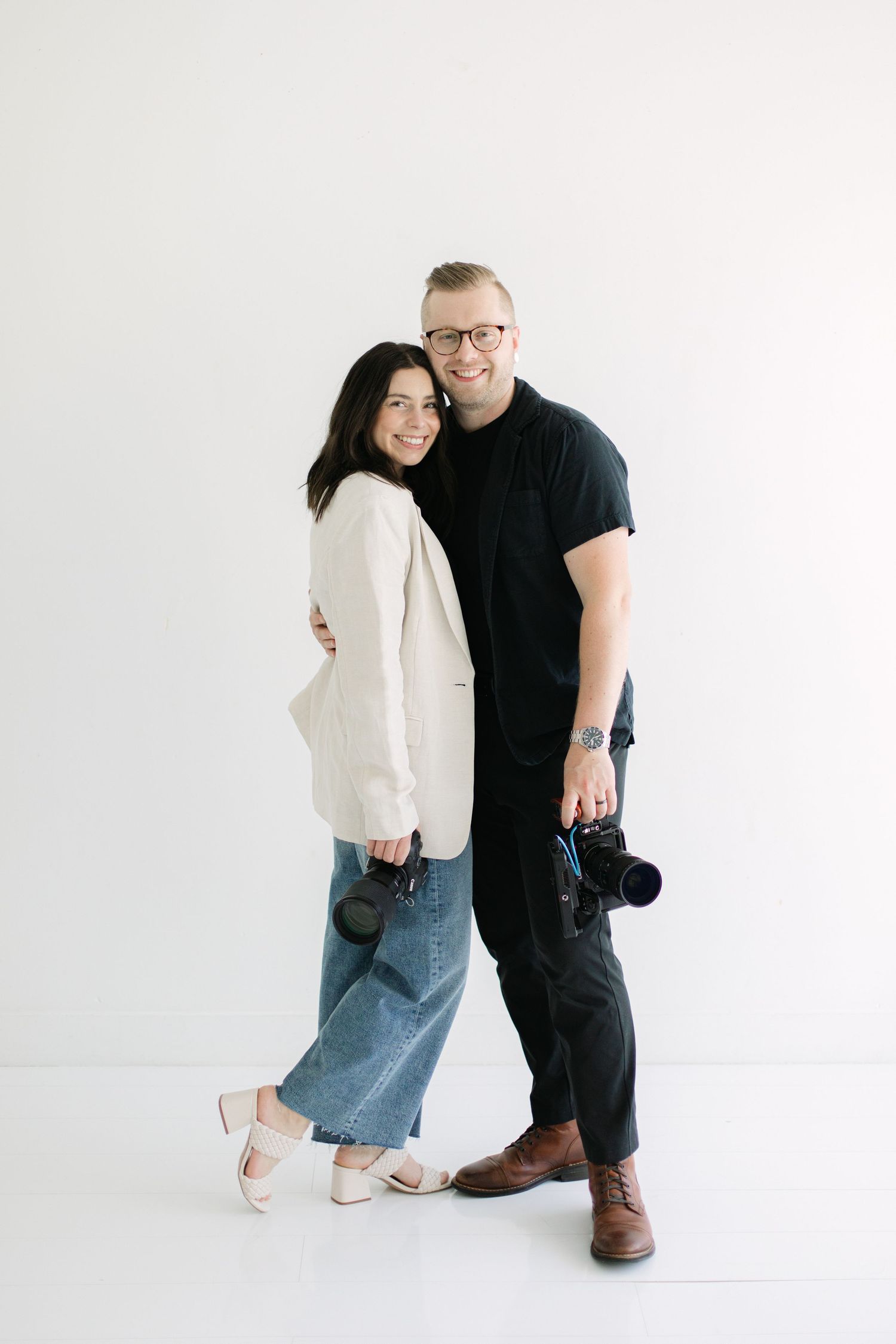 Two people pose together in a bright white studio wearing casual outfits with matching warm expressions.
