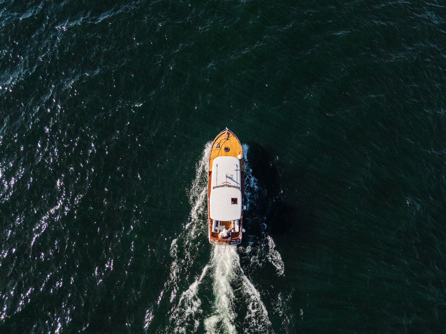 Aerial view of a small white and yellow boat cruising through dark green ocean waters, leaving a white wake trail.