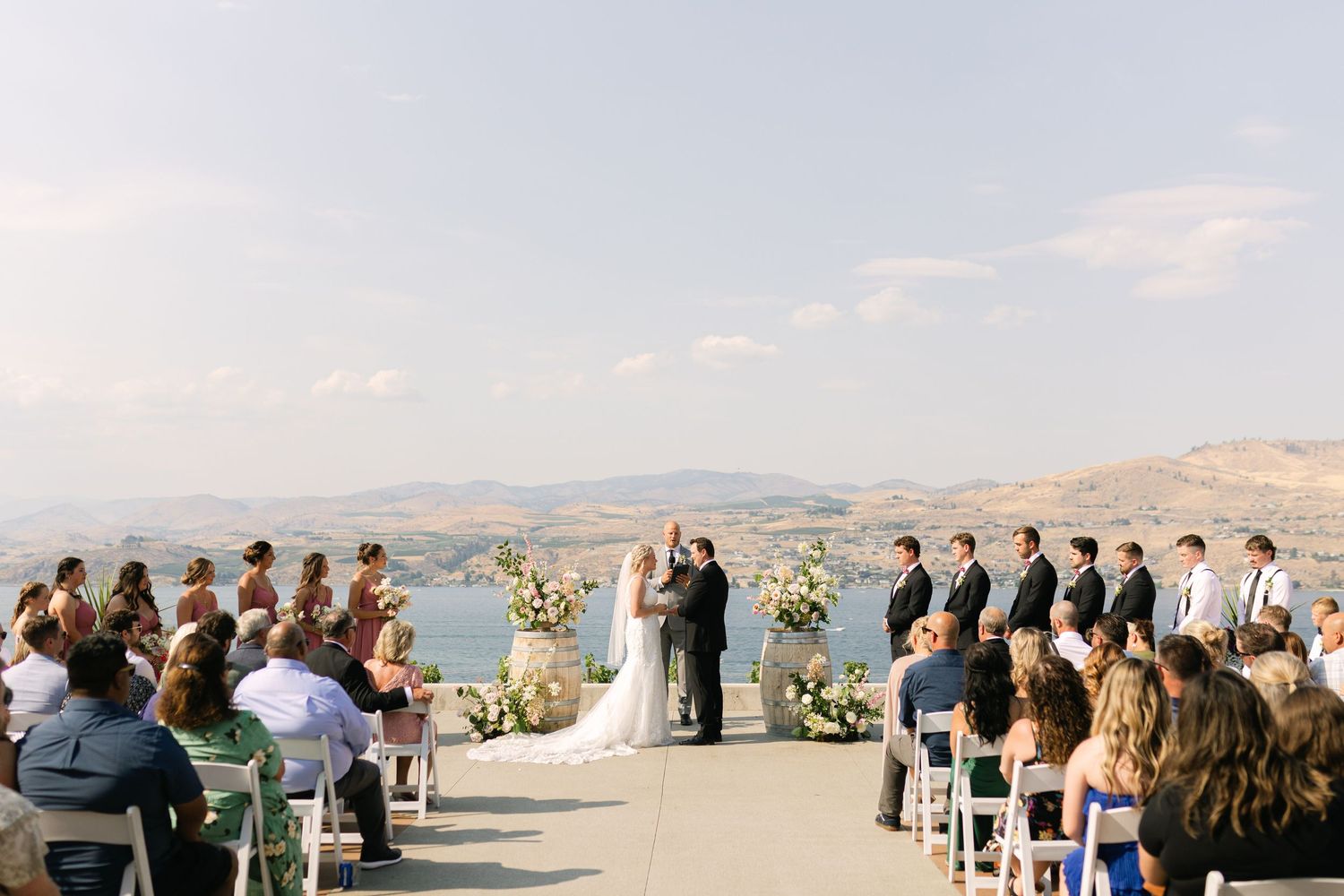 Outdoor wedding ceremony overlooking a scenic mountain landscape with guests seated on white chairs.