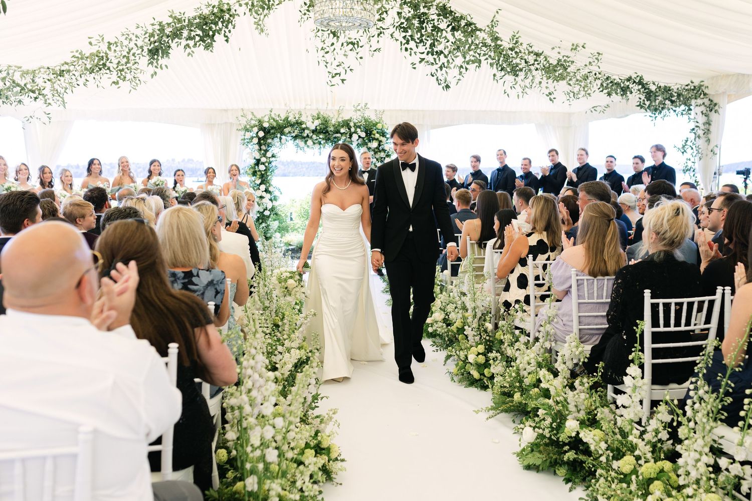 Wedding ceremony space decorated with greenery and white chairs under an elegant outdoor tent.