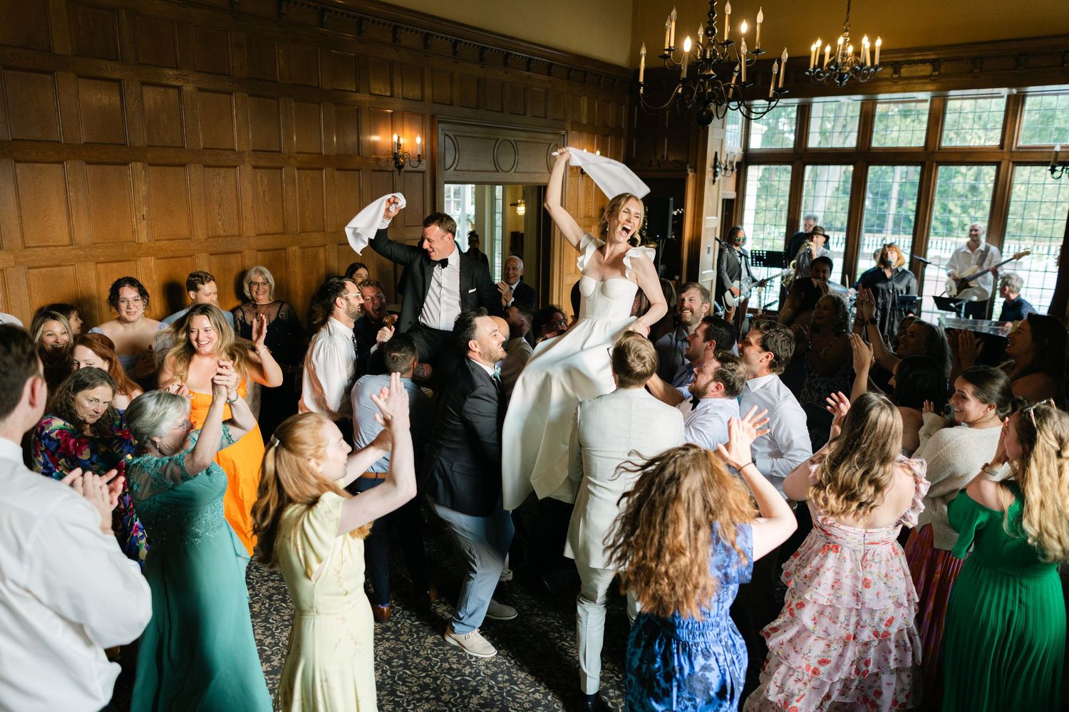 Wedding reception guests dancing and celebrating under chandelier lighting indoors.
