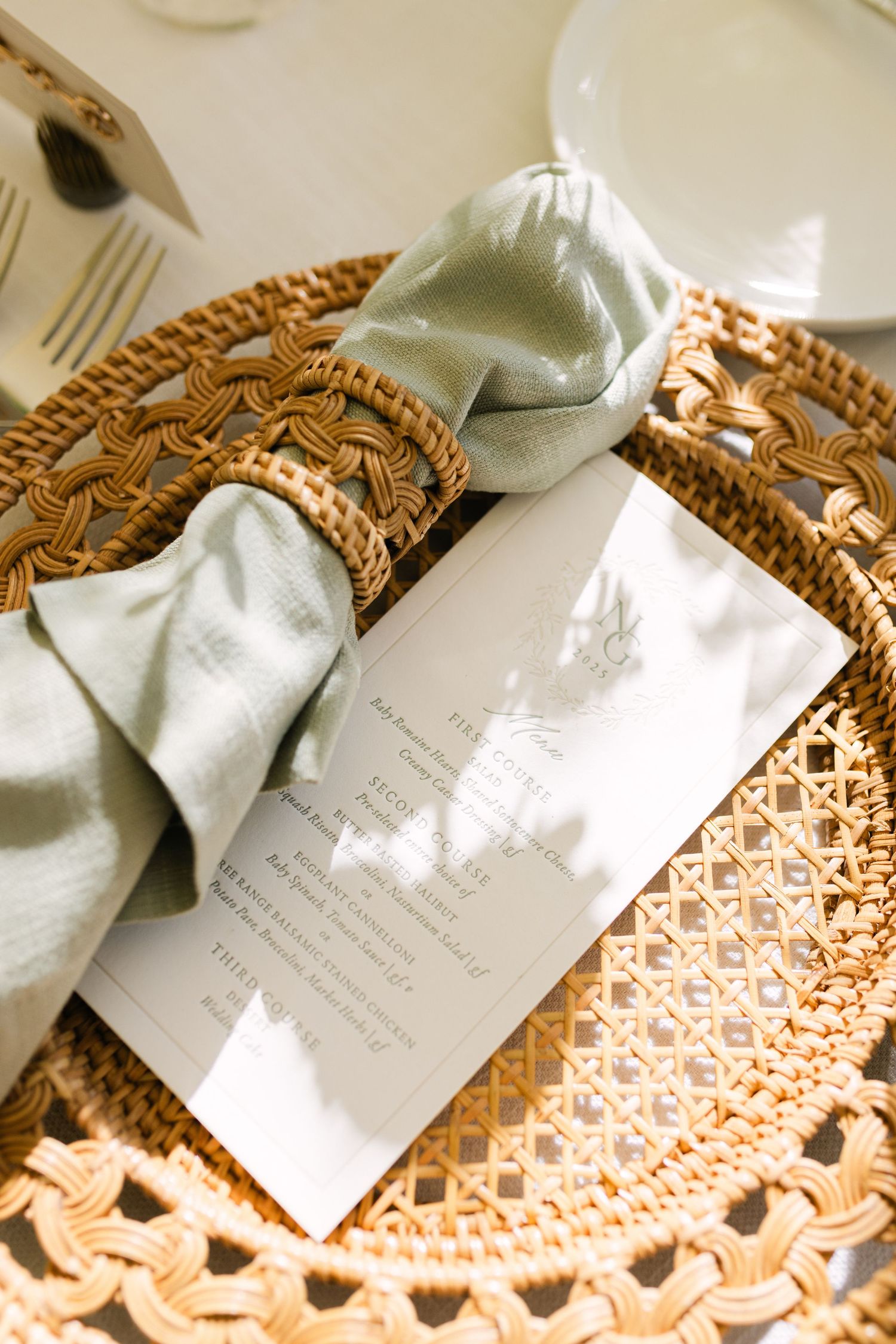 Wedding invitation with sage green bow displayed on woven charger plate.