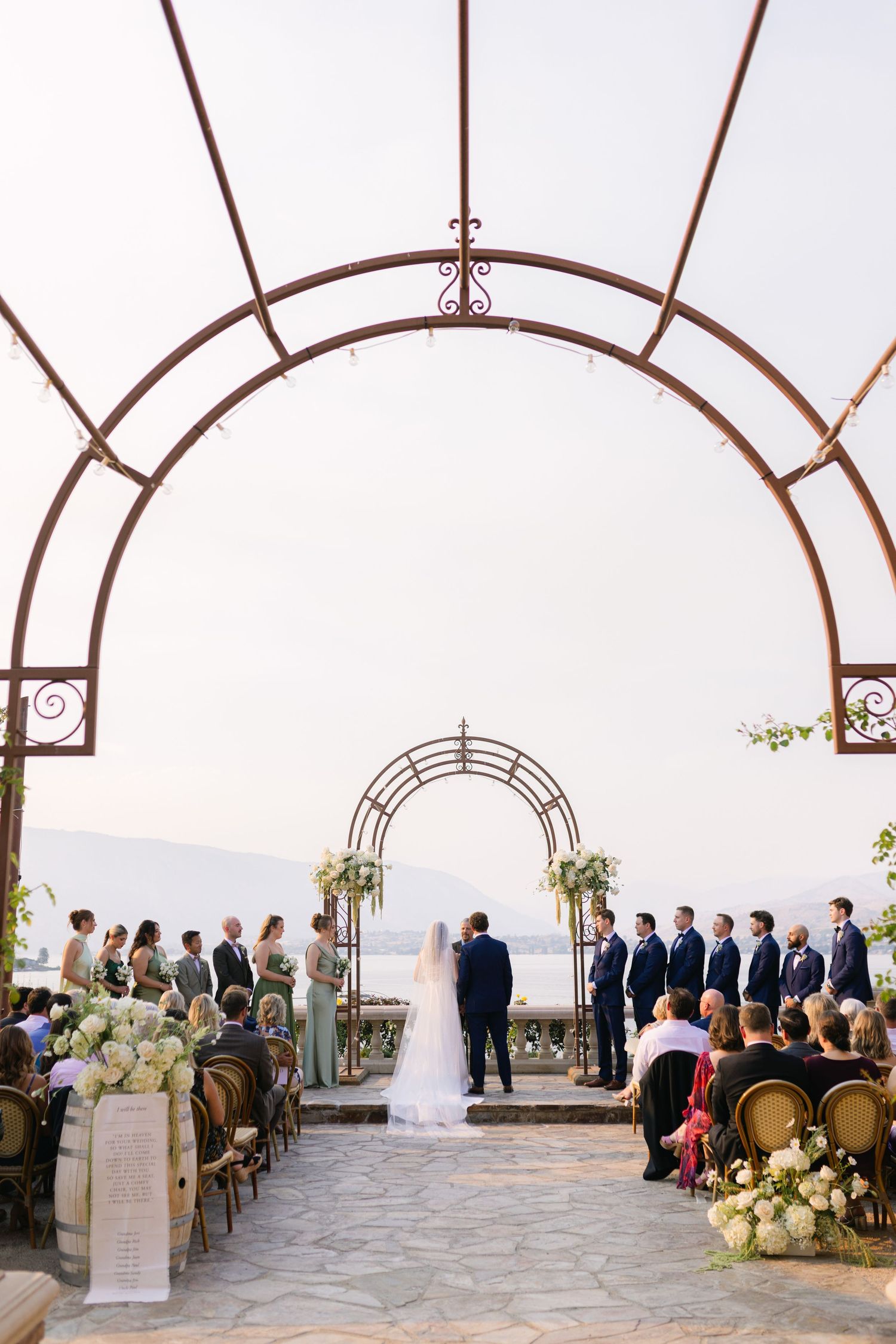 Outdoor wedding ceremony setup under arched metal pergola with mountain views.