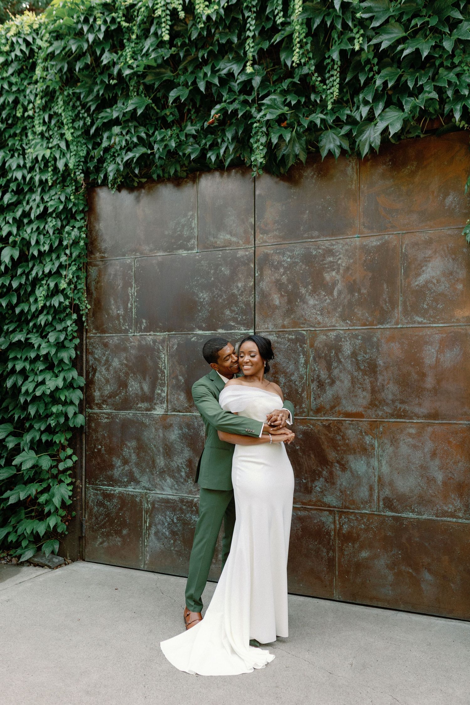 A couple embraces against an ivy-covered metal wall during their wedding photoshoot.