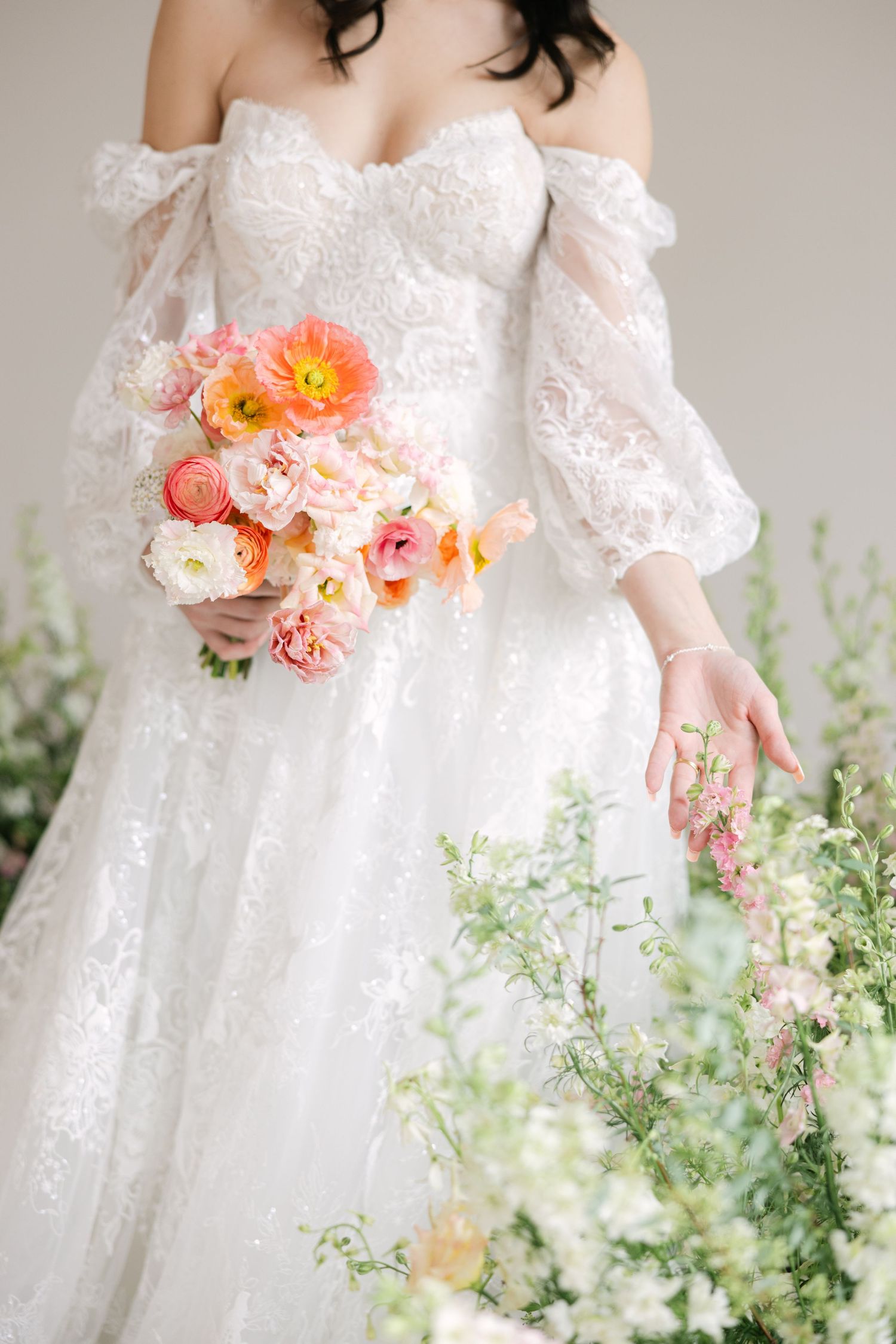 A romantic wedding dress with off-shoulder lace sleeves and a peach and coral floral bouquet against delicate greenery.