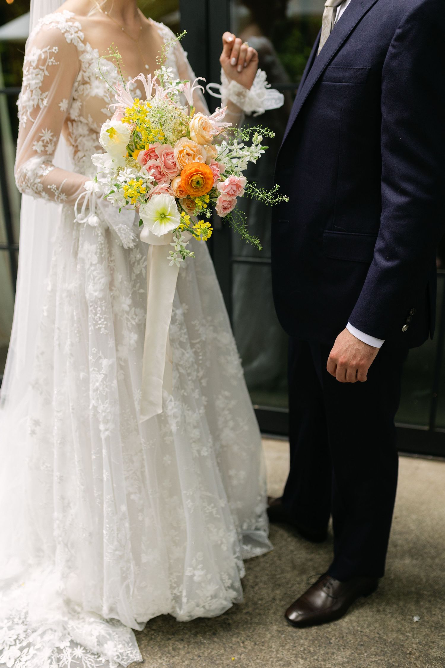 Close-up of wedding attire showing white lace dress details and colorful floral bouquet.
