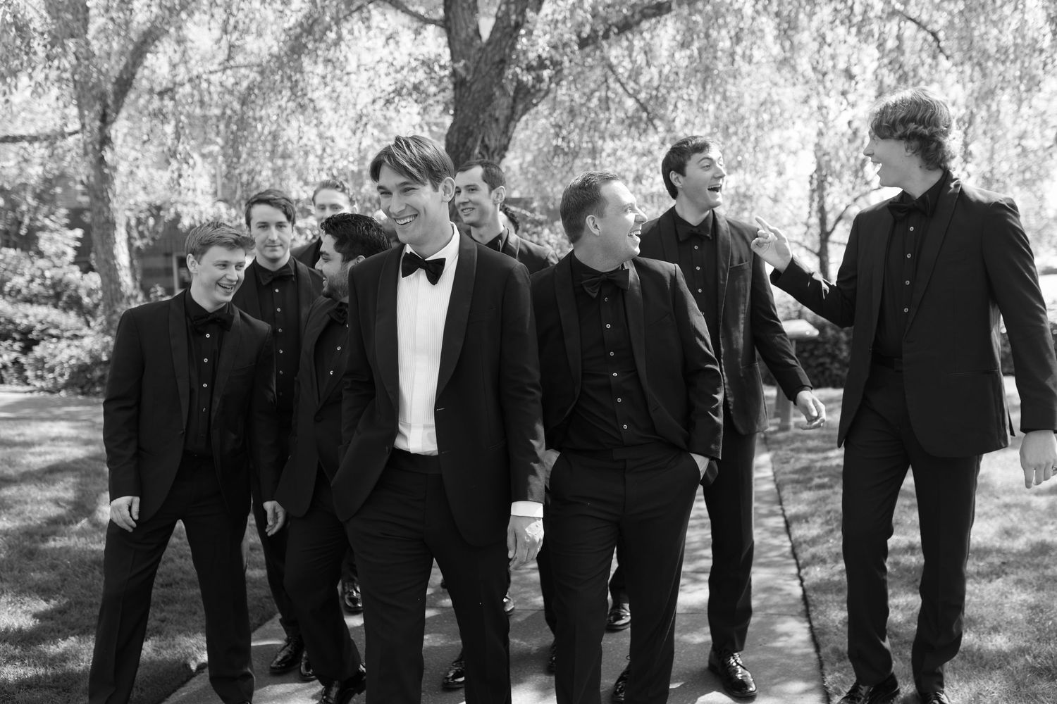 Groomsmen in black suits pose together outdoors in a candid sequence of black and white photos.