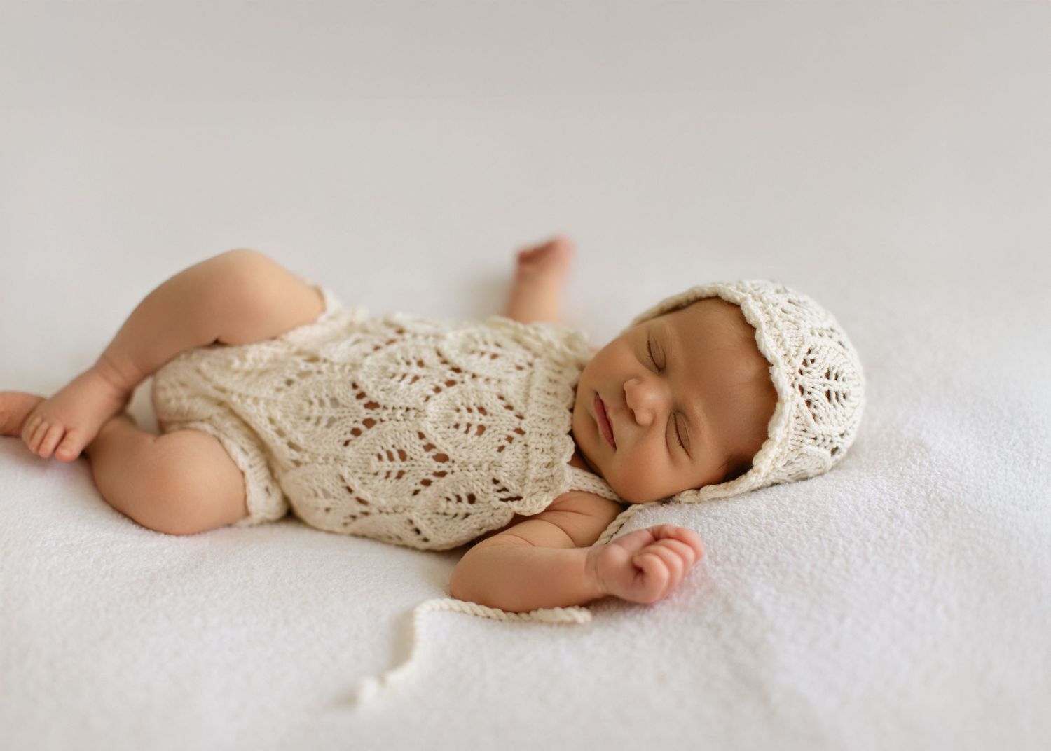 Sleeping newborn in delicate crochet wrap on white backdrop.