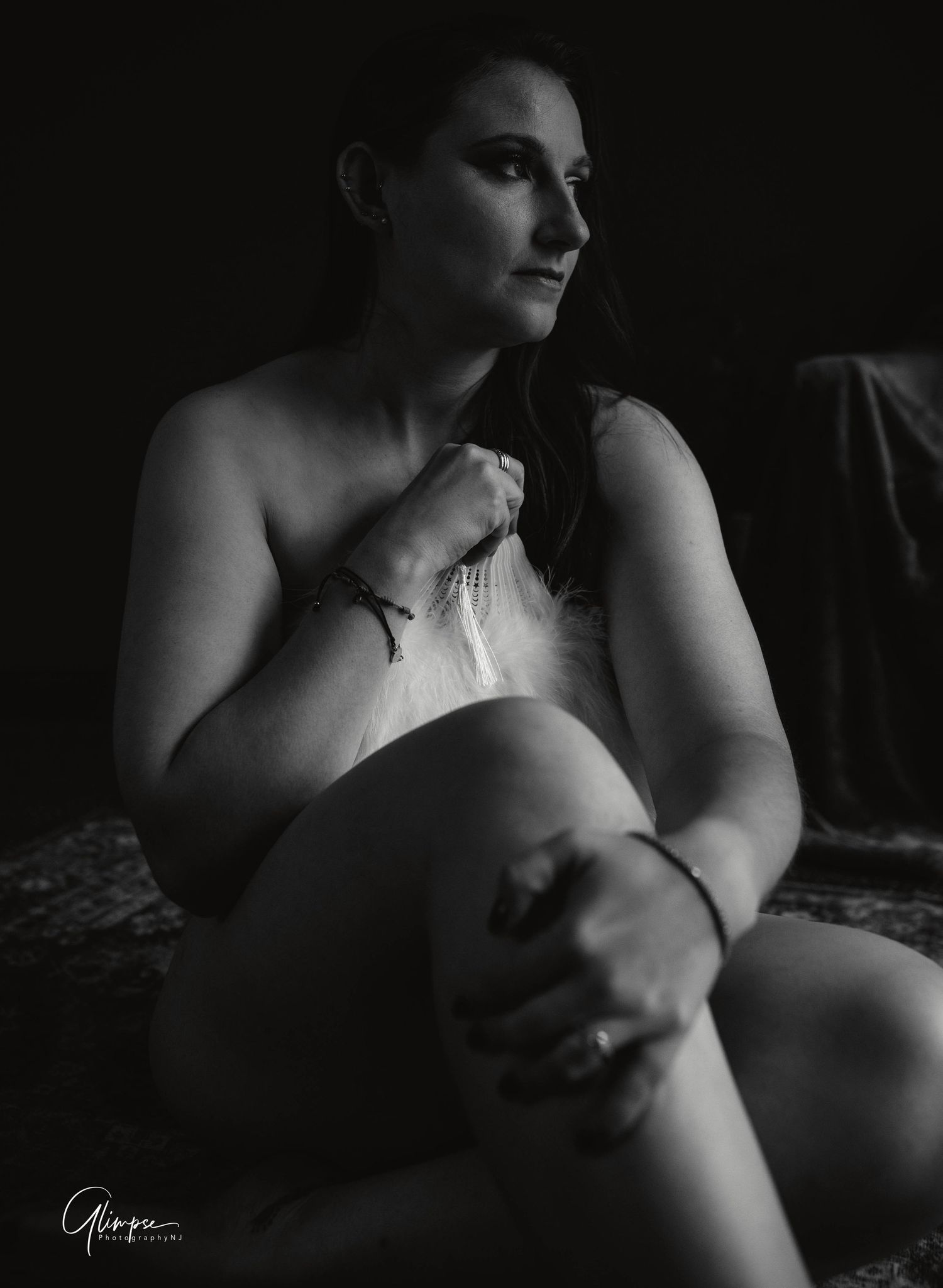 Black and white boudoir portrait of a woman sitting and gazing away in soft light.