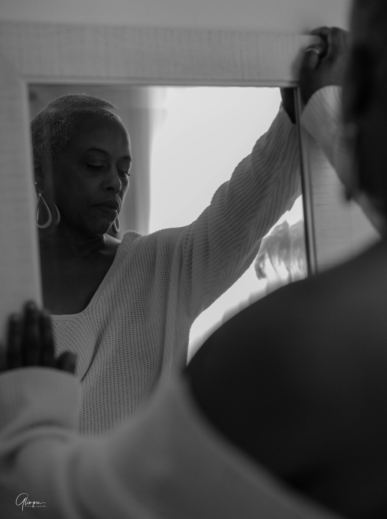 Black and white artistic portrait of a woman reflected in a mirror in soft light.