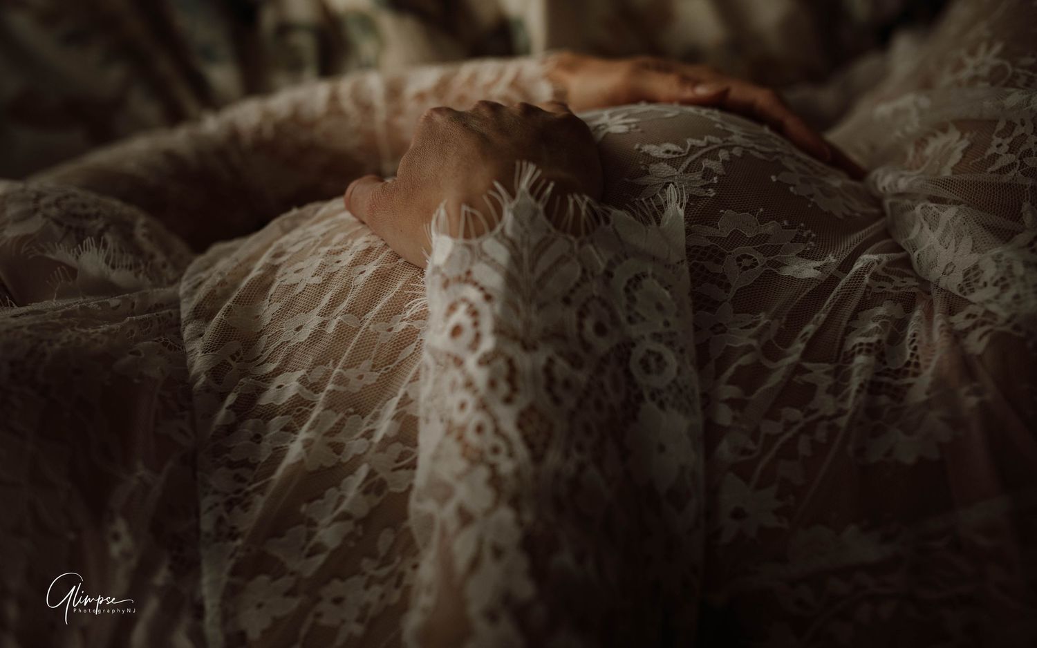 Artistic close-up of hands resting on a lace fabric in warm dark moody tones for a boudoir session.