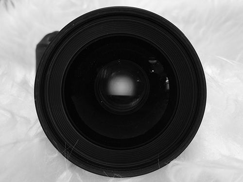 Close up view of a black camera lens against white background.