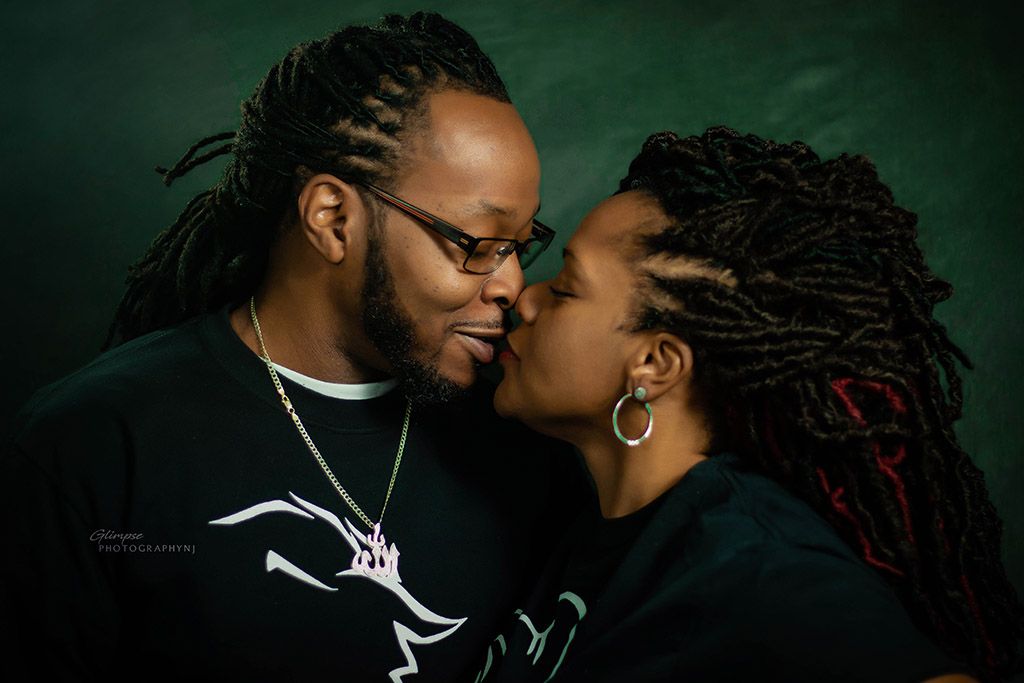 A tender and intimate portrait of a couple sharing an affectionate moment against a dark green background.