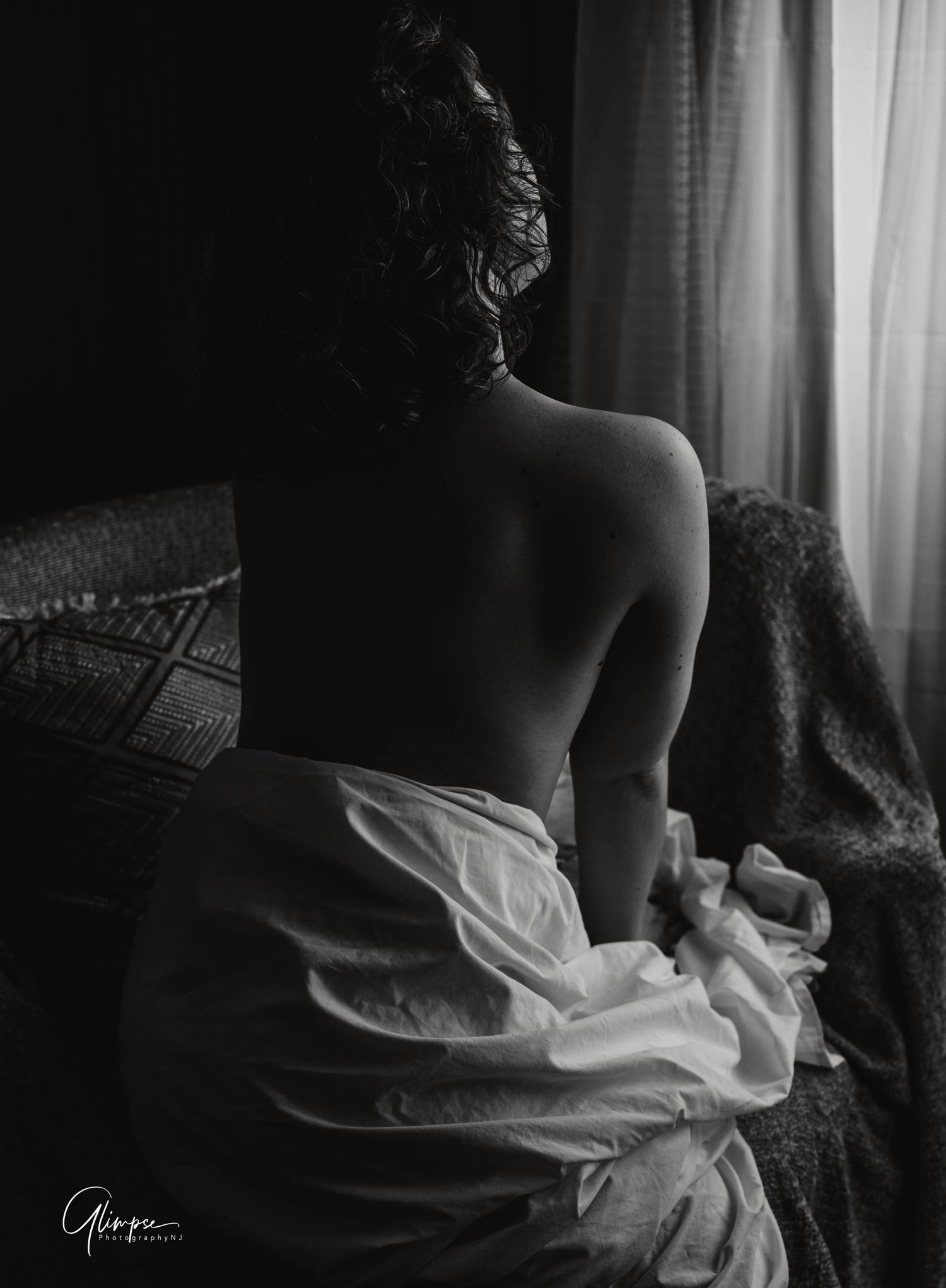 Black and white artistic boudoir photo of a woman's bare back near a window.