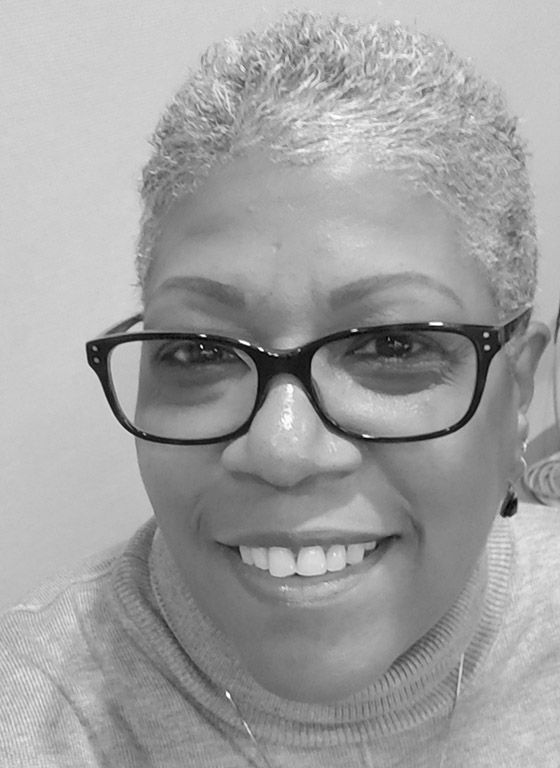 Black and white selfie portrait of a smiling woman with short gray hair and glasses.