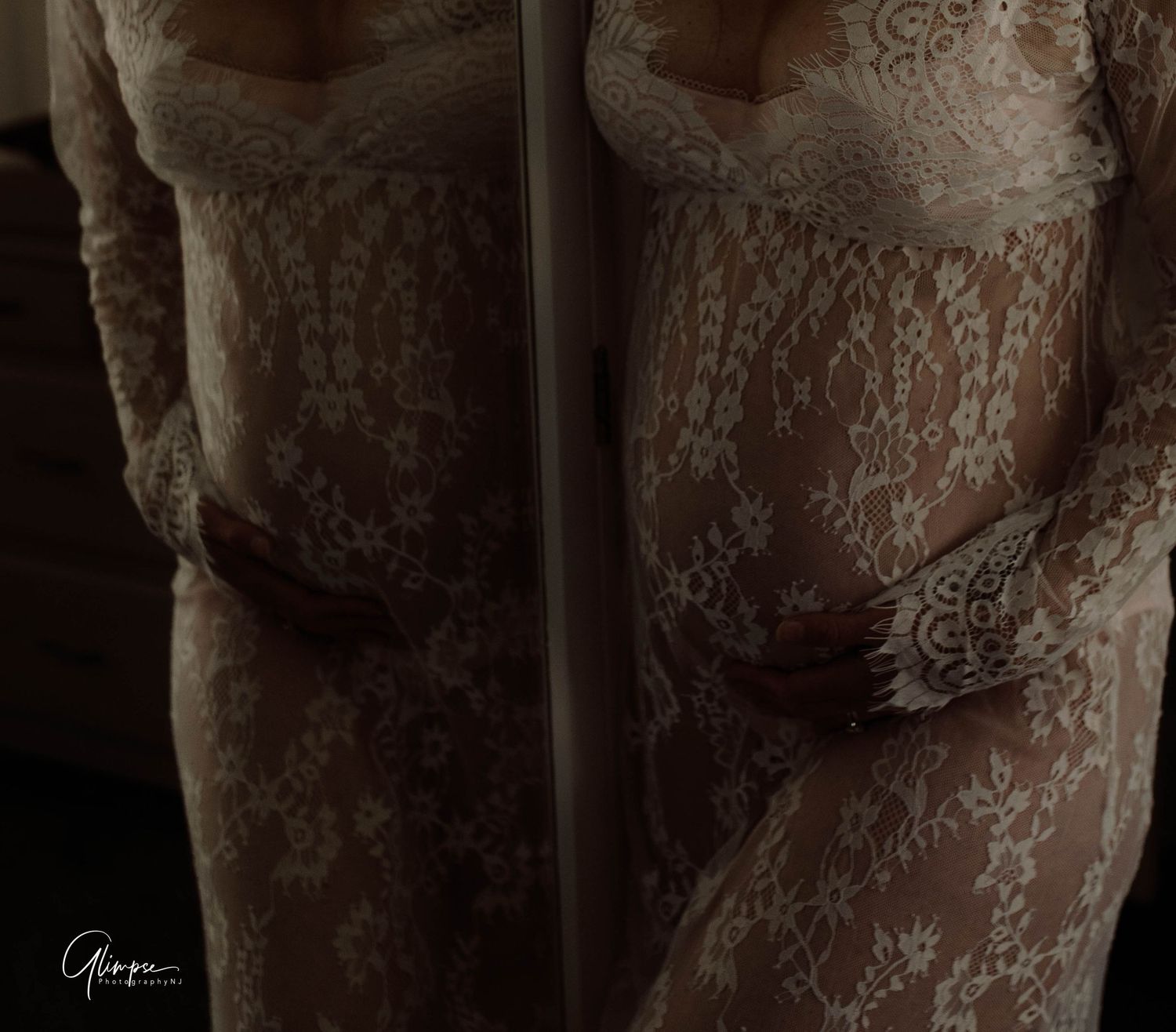Close-up of a pregnant woman's baby bump in a sheer white lace dress with dramatic moody lighting.